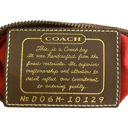Close-up of a Coach leather tag on a brown bag, featuring gold-embossed lettering and a orange fabric lining visible at the sides.