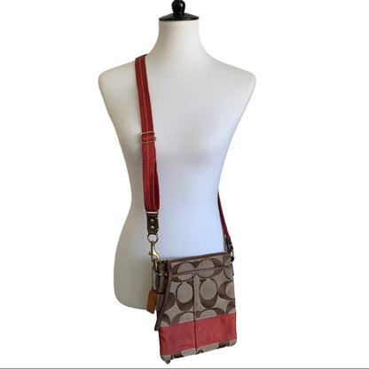 A Coach crossbody bag in signature monogram canvas with orange trim and strap, displayed on a white mannequin torso against a white background.