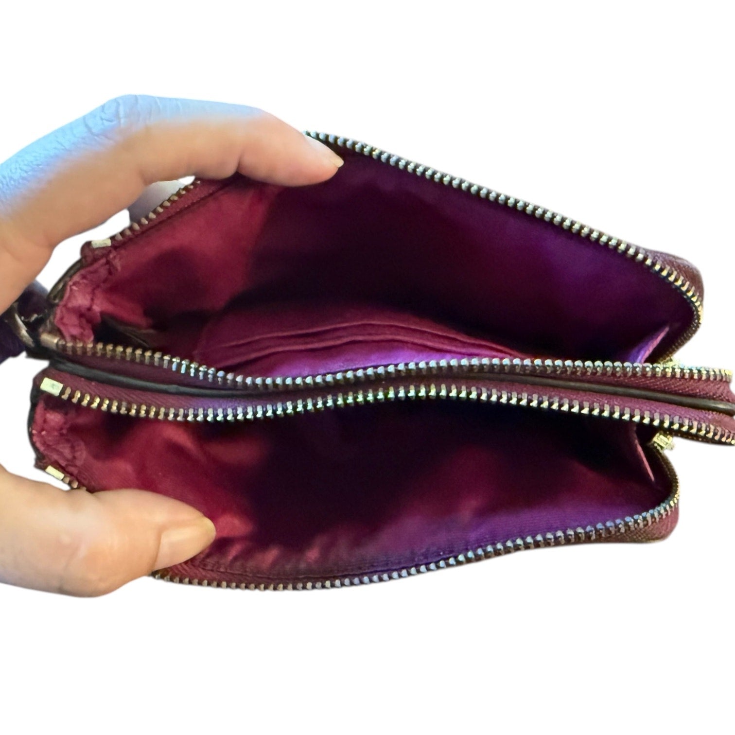 Interior of clutch bag with a zipper held open by a hand on a white background