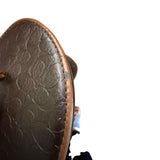 Close-up of a brown leather shoe with embossed pattern and issues on the edges on a white background