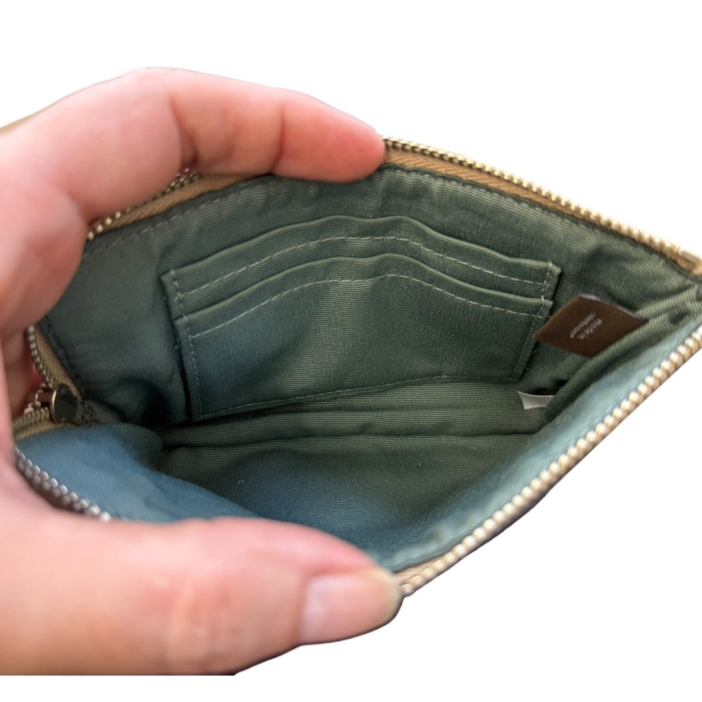 Hand holding an open a pouch with green interior with a visible brand label and pockets on a white background