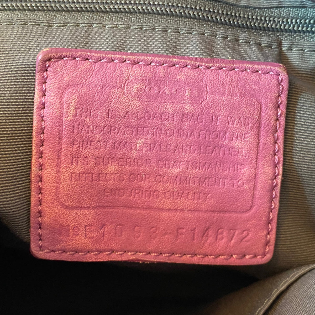 A close-up of a purple leather Coach interior label sewn onto an olive green fabric bag.
