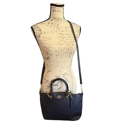 A Coach handbag in black leather , displayed on a beige script-patterned dress form mannequin against a white background.