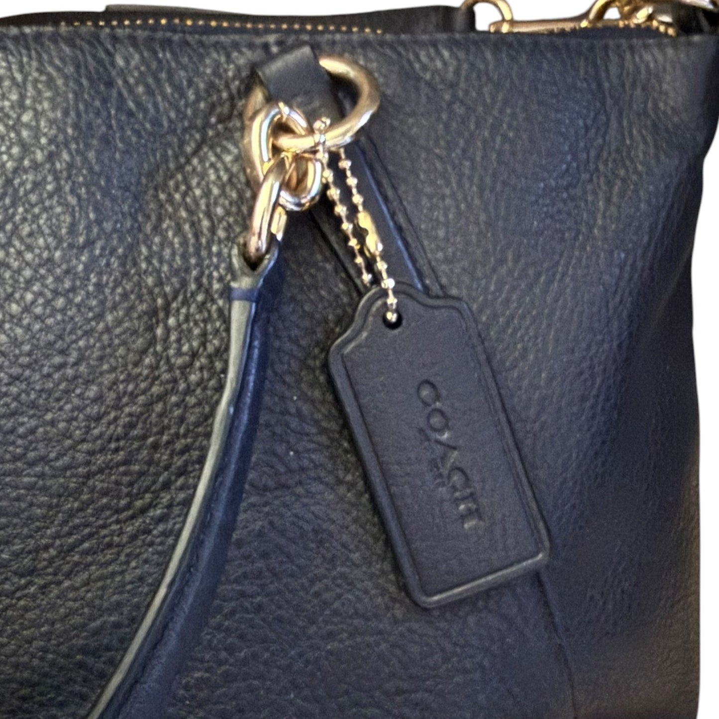 Close-up of a black pebbled leather handbag with gold-tone hardware, a black strap, and a black Coach logo tag hanging from a ring.