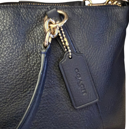 Close-up of a black pebbled leather handbag with gold-tone hardware, a black strap, and a black Coach logo tag hanging from a ring.
