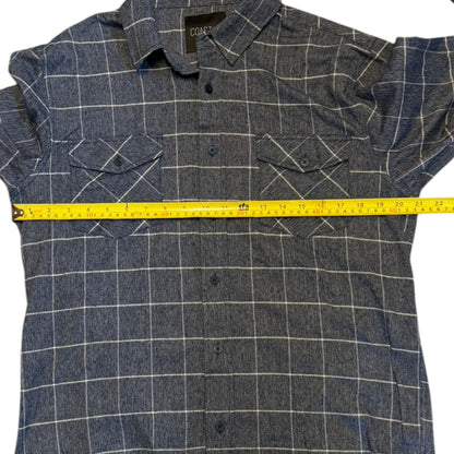 A blue button-up shirt with a yellow measuring tape stretched horizontally across the chest to show the width, photographed on a white background.