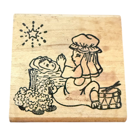 Wooden stamp with a design someone praying over a baby sleeping on a bed.
