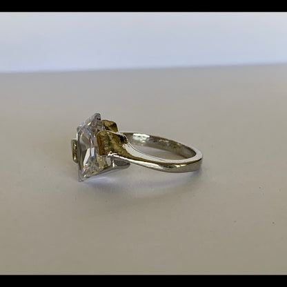 Side of silver ring with a large faux diamond on a light background