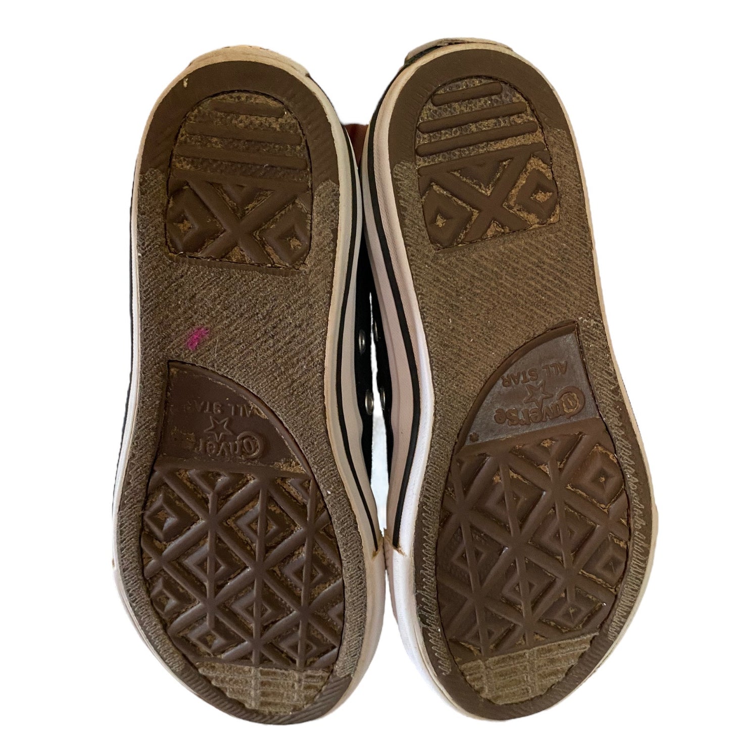 A pair of Converse sneakers shown from the bottom, displaying the brown textured rubber outsoles with the Converse logo , set against a plain white background.