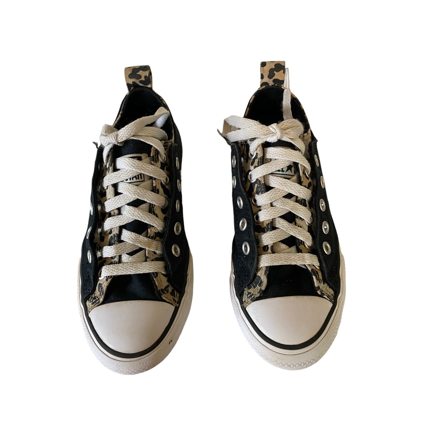 A pair of black low-top canvas sneakers with beige and black leopard print panels, white laces, and white rubber toe caps, shown from a top-down view on a white background.
