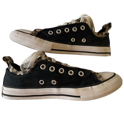 A pair of low-top canvas sneakers in black with a leopard-print pattern panel, white laces, and off-white rubber soles.