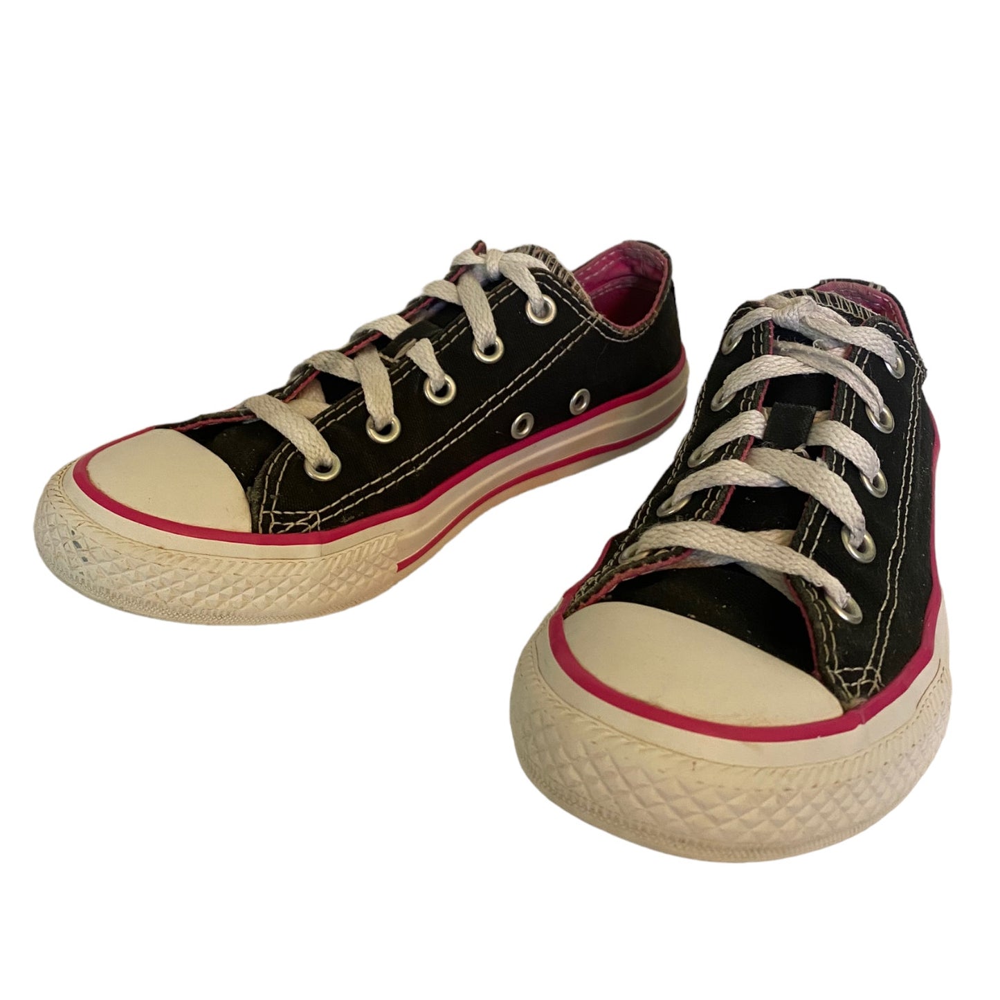 A pair of black canvas low-top sneakers with white laces, cream rubber toe caps and soles, and a pink stripe detail on the sidewall, shown against a plain white background.