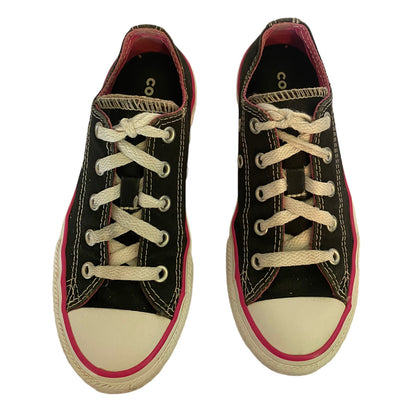 A pair of black canvas low-top sneakers with white laces, white toe caps, and a thin pink stripe along the edge of the sole, shown from a top-down view on a white background.