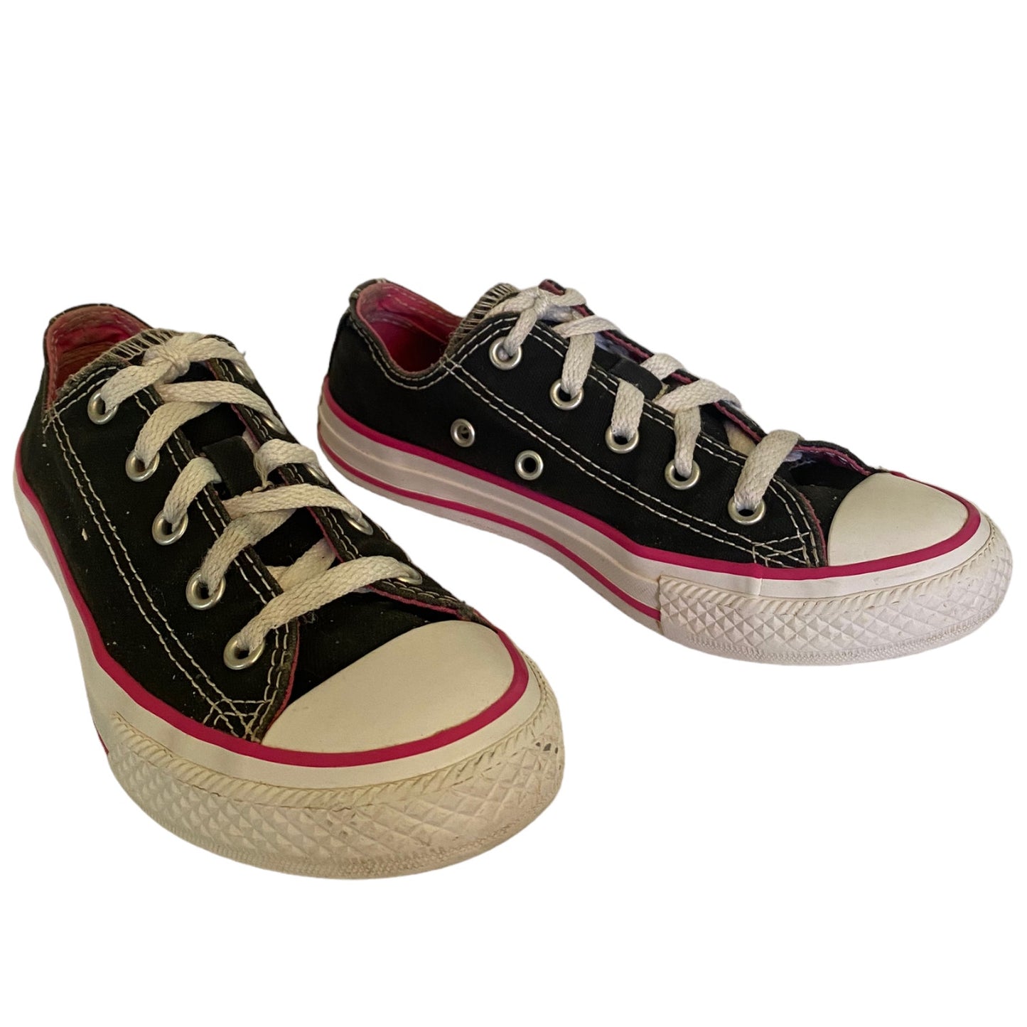A pair of black canvas low-top sneakers with white laces, white rubber toe caps and soles, and a thin pink stripe along the side, shown on a plain white background.