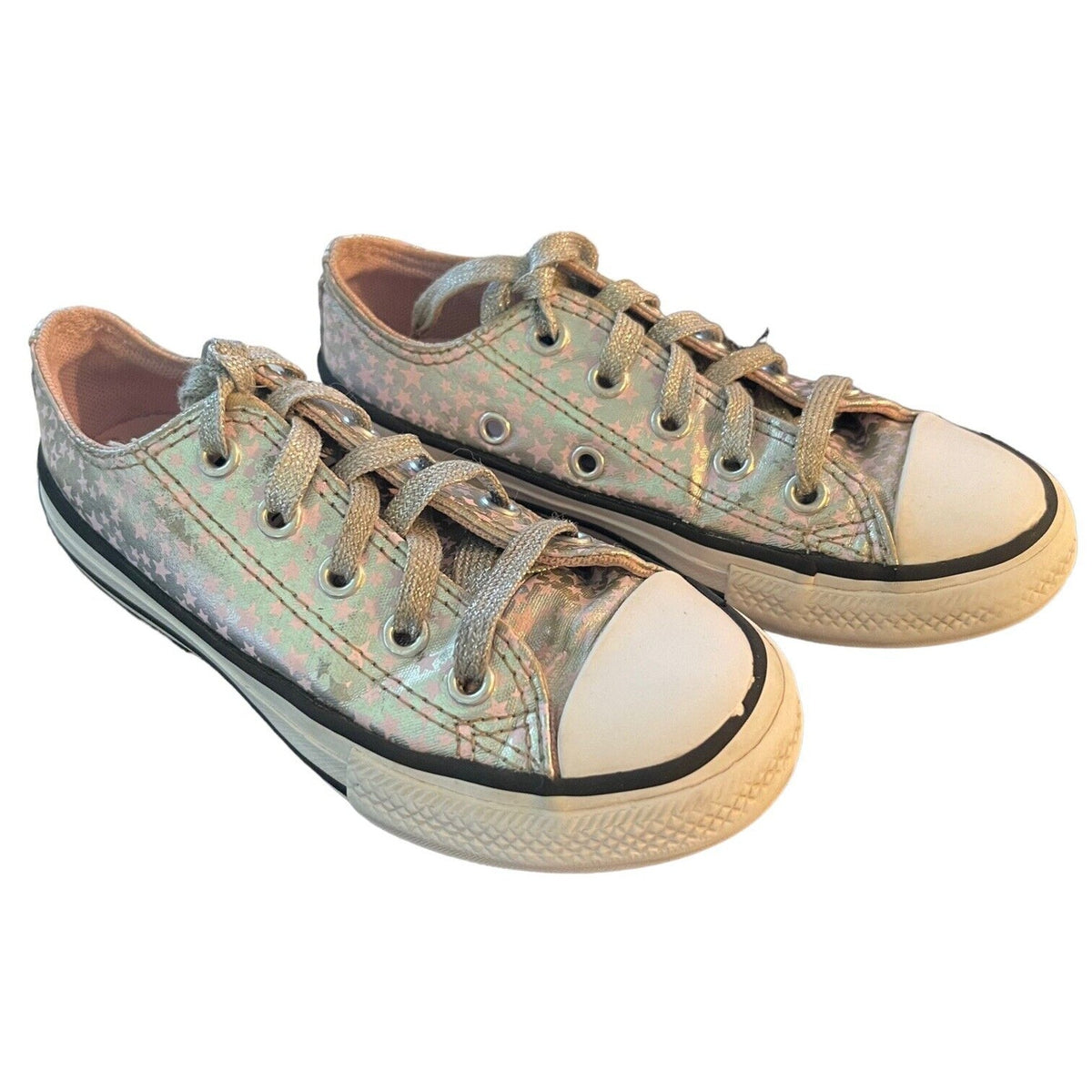A pair of low-top canvas sneakers with an iridescent, holographic finish. The shoes feature off-white rubber toe caps and soles, black rubber trim, and matching metallic laces, shown against a plain white background.