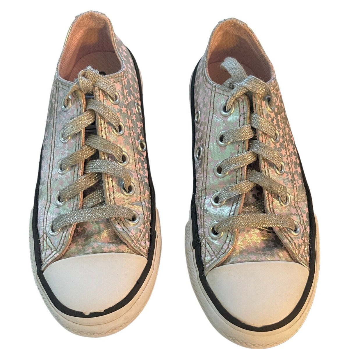 A pair of low-top canvas sneakers with an iridescent metallic silver star pattern, featuring white rubber toe caps and black trim, shown against a plain white background.