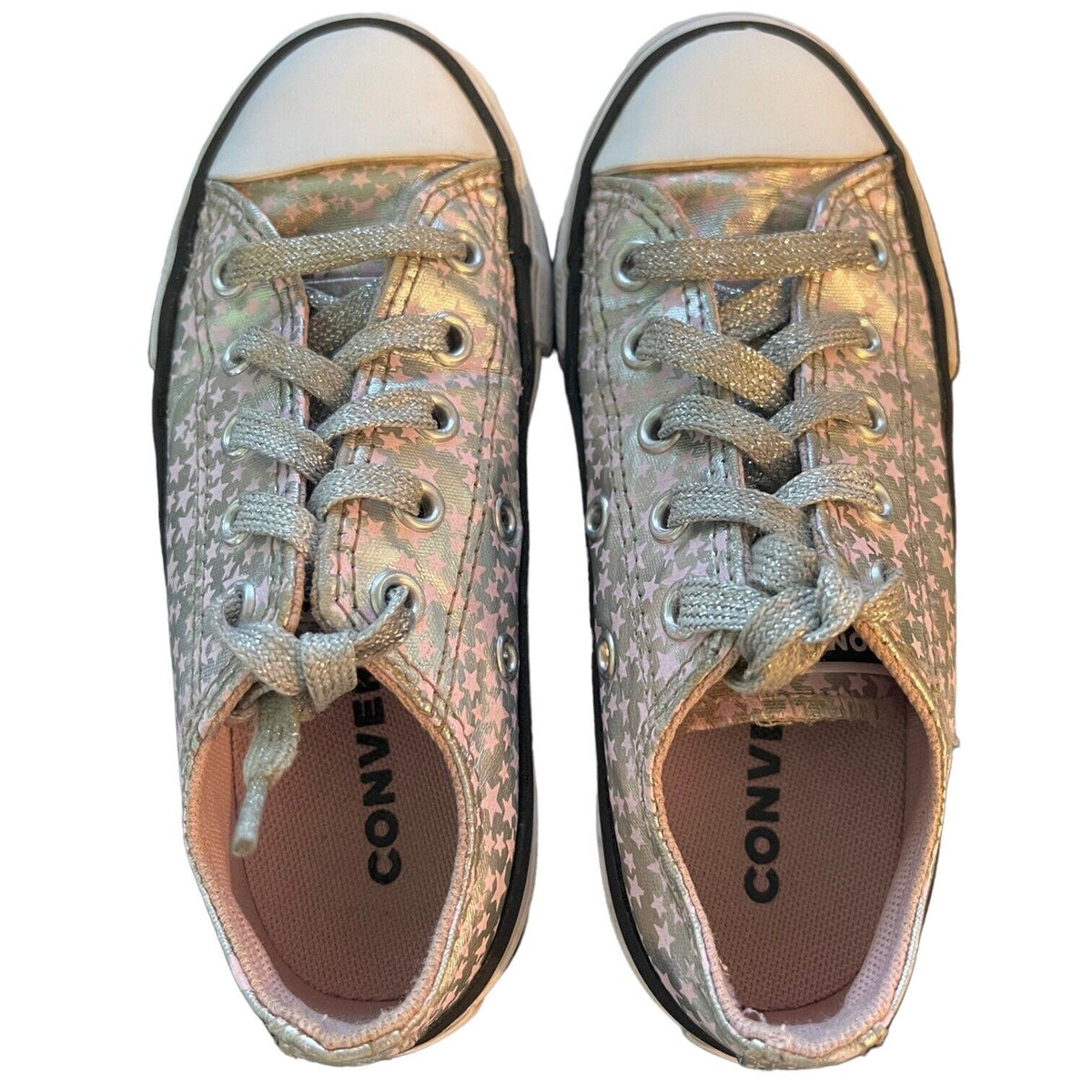 A pair of Converse low-top sneakers with a metallic silver and pink holographic glitter canvas upper, matching glitter laces, and a white rubber toe cap, shown from a top-down view on a white background.