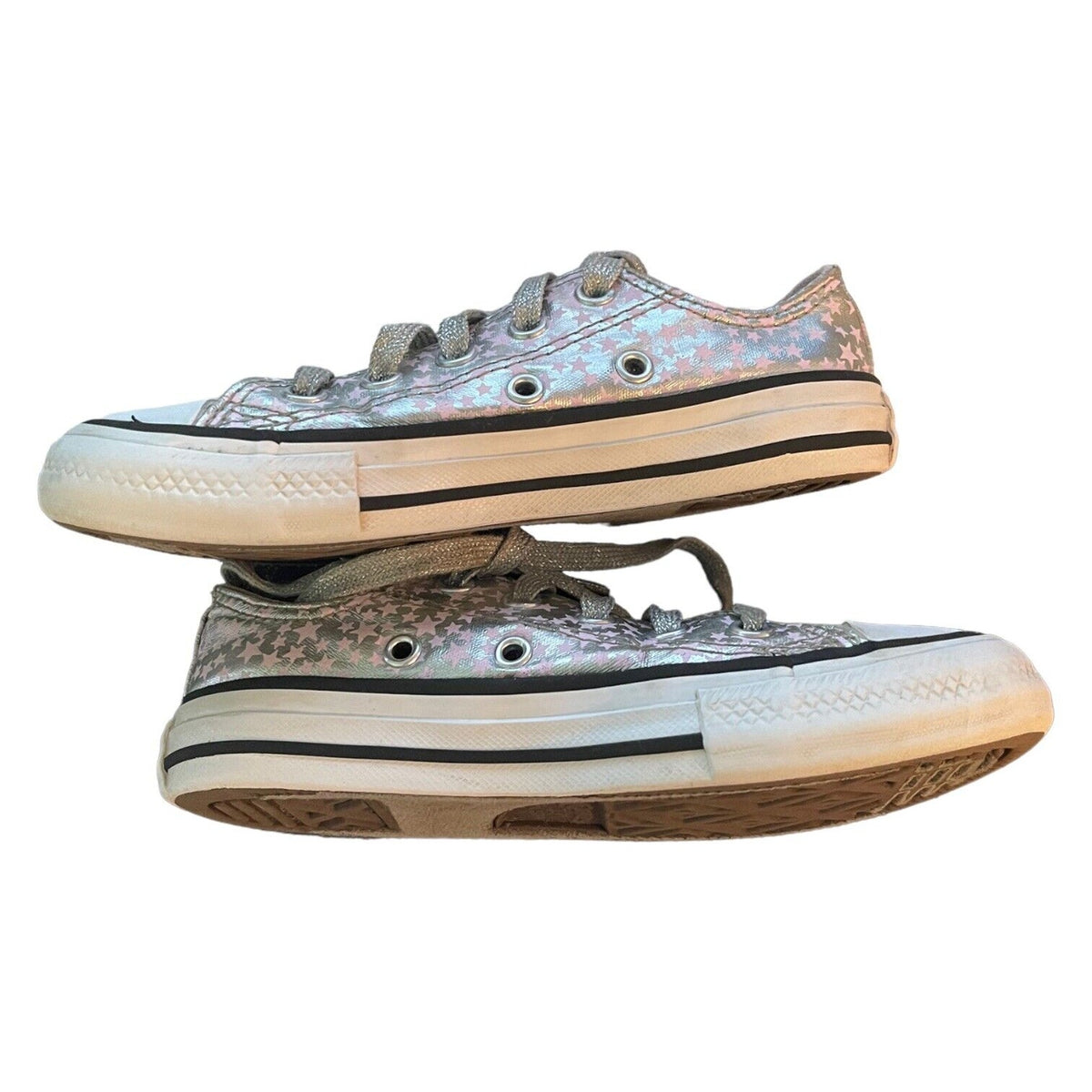 A pair of low-top canvas sneakers with an iridescent silver pink finish, featuring gray laces, silver eyelets, a white rubber midsole with a black stripe, and a brown outsole, shown against a plain white background.