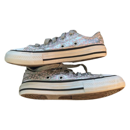 A pair of low-top canvas sneakers with an iridescent silver pink finish, featuring gray laces, silver eyelets, a white rubber midsole with a black stripe, and a brown outsole, shown against a plain white background.