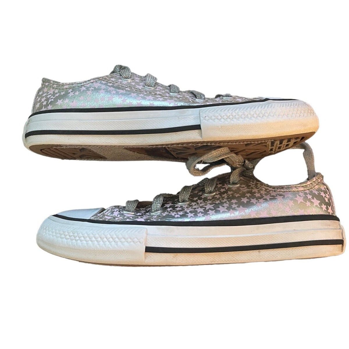 A pair of low-top canvas sneakers with an iridescent silver pink finish, featuring a white rubber sole with black stripes and gray laces.