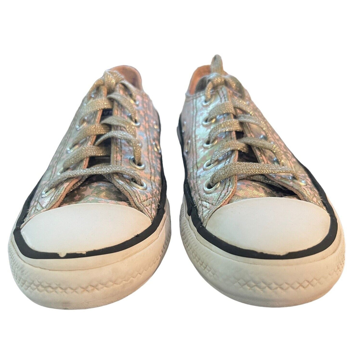 A pair of low-top canvas sneakers with a metallic silver and iridescent pattern, featuring white rubber toe caps, black trim, and white laces, shown against a plain white background.