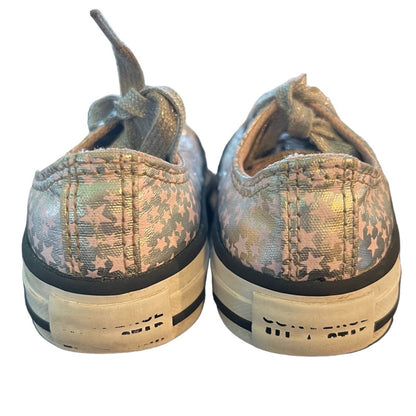 A pair of Converse low-top sneakers shown from the back, featuring a metallic silver and pink star pattern with star details, off-white rubber soles, and black stripes.