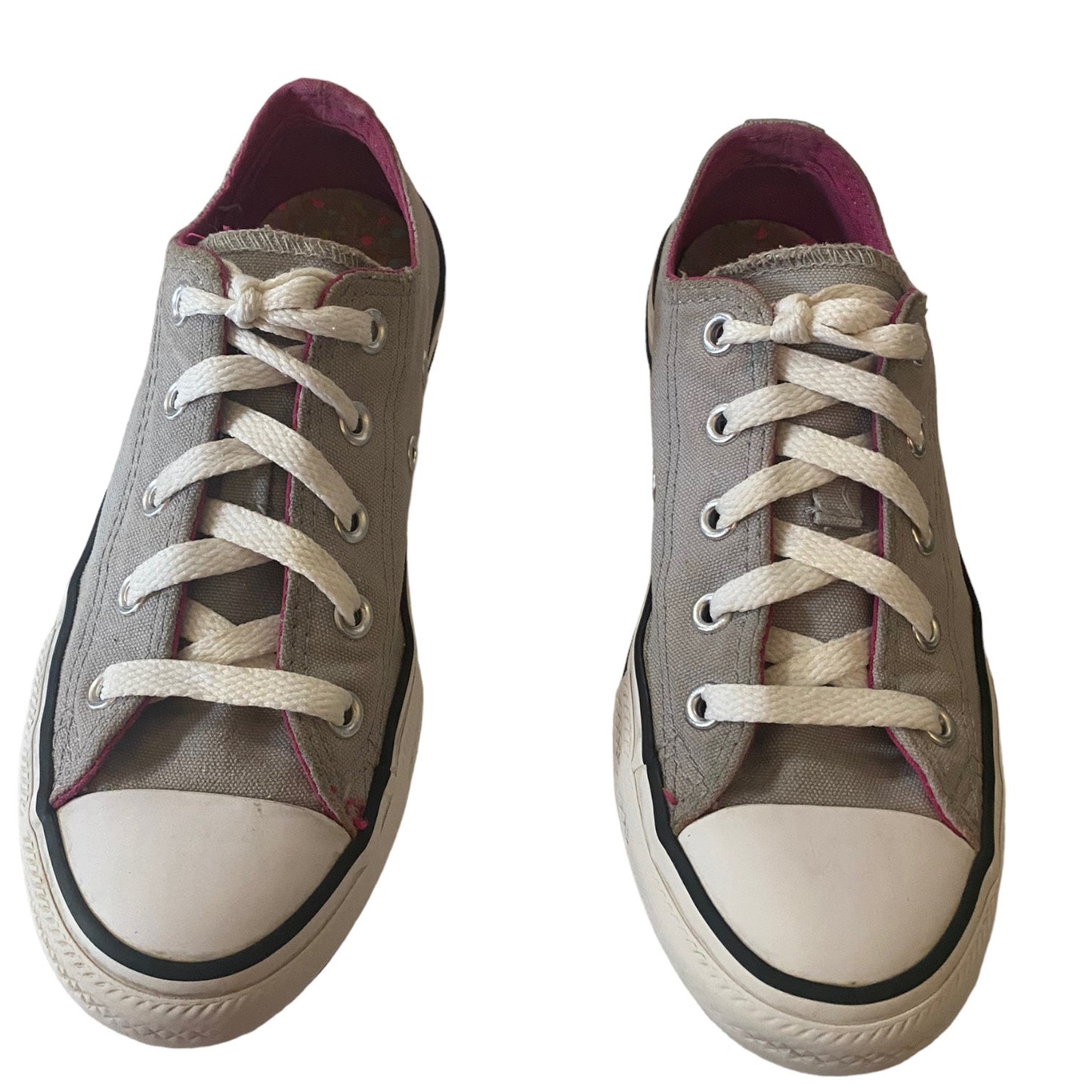 A pair of low-top canvas sneakers in a  gray color, featuring white laces, white rubber toe caps, and black rubber trim around the soles. The interior lining is a dark magenta.
