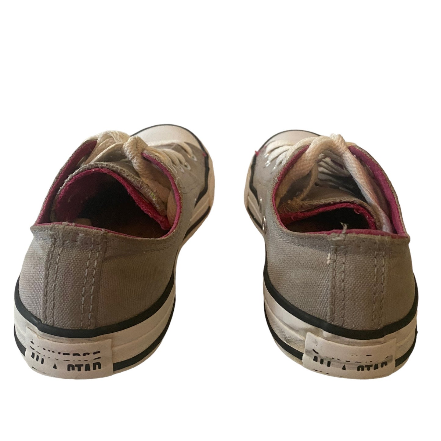 A pair of Converse All Star low-top canvas sneakers shown from the back, featuring a light gray canvas upper, white rubber soles, and a pink inner lining.