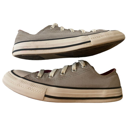 A pair of classic low-top canvas sneakers in a gray color, featuring white laces, a black stripe detail on the midsole, and a cream-colored rubber toe cap and sole.