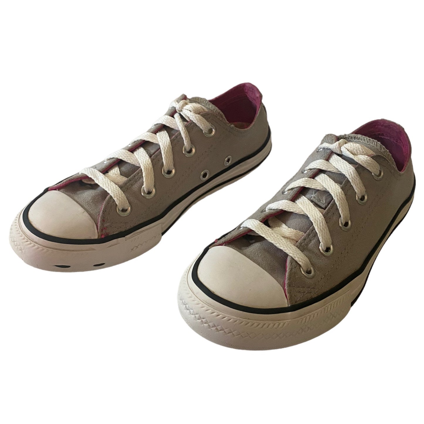 A pair of low-top canvas sneakers in a gray color, featuring white laces, a white rubber toe cap, and a black stripe around the collar. The interior lining is a contrasting magenta pink.