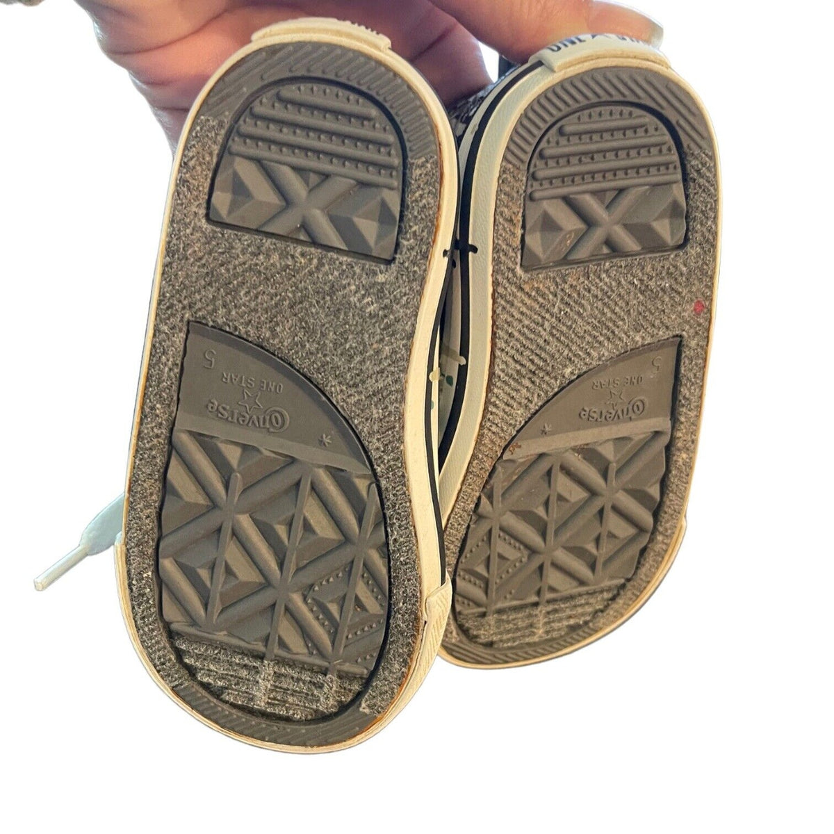 A close-up of the soles of Converse sneakers held up by a hand against a white background.