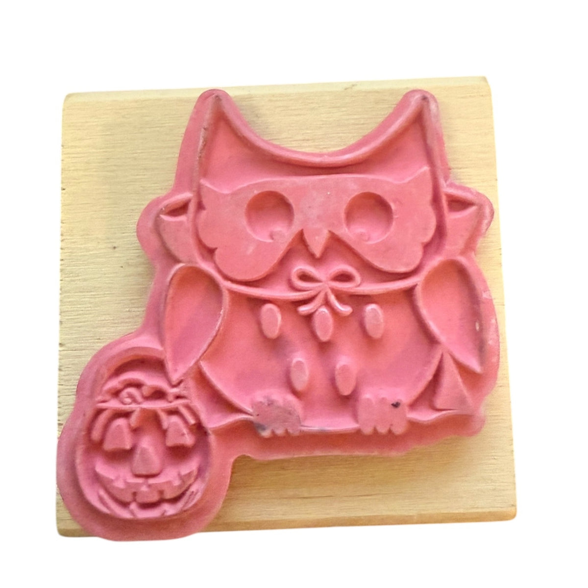 A pink owl-shaped rubber stamp with a carved pumpkin detail, mounted on a light-colored wooden block against a white background.