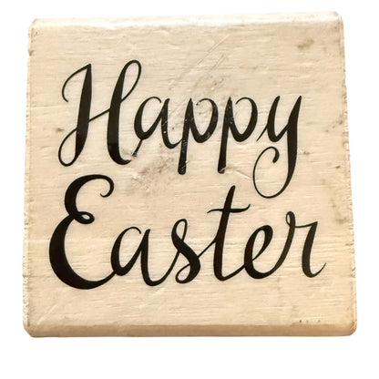 A wood block rubber stamp and the words 'Happy Easter' written in black cursive script, shown on a plain white background.