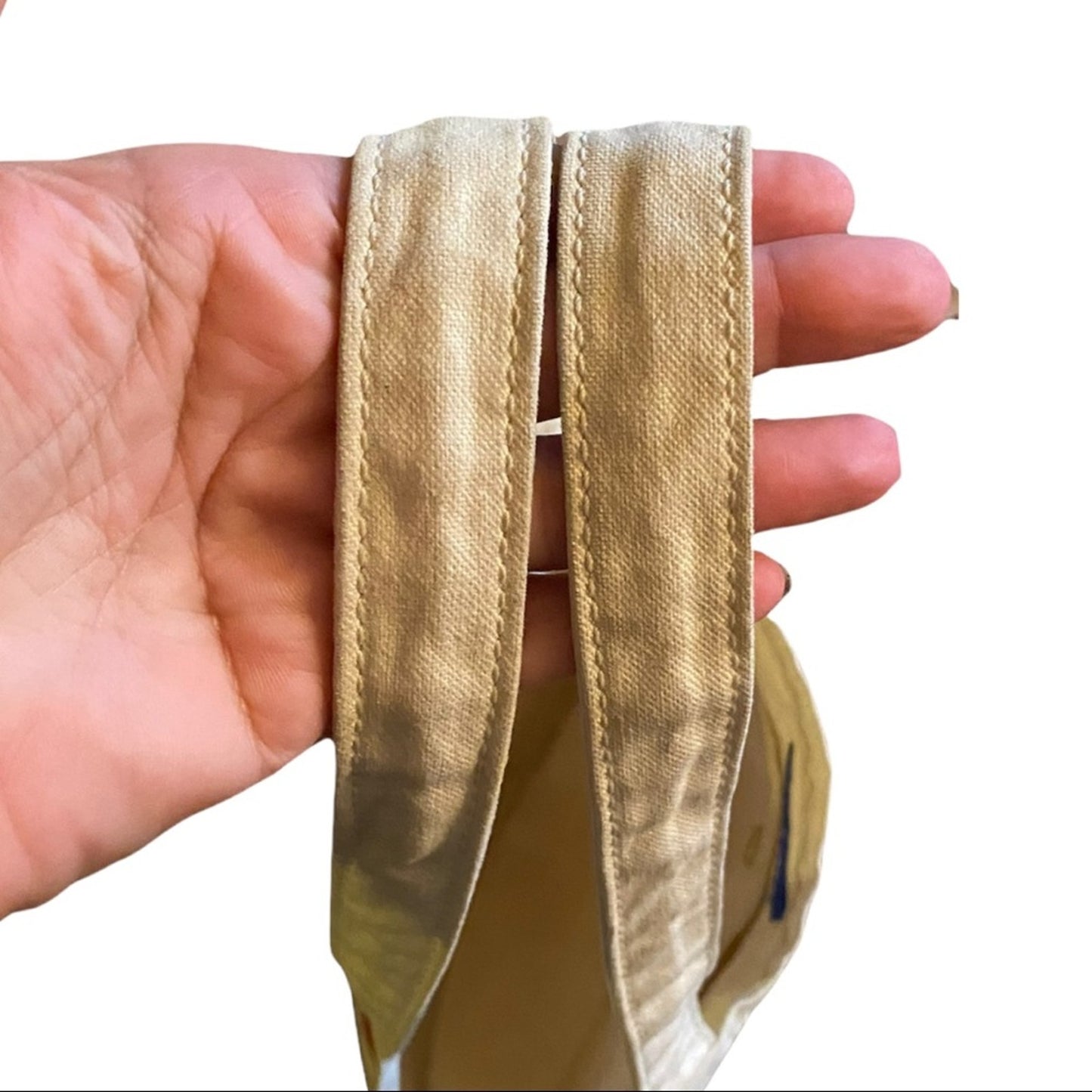 A close-up of a hand holding the handles of a canvas tote bag against a plain white background.