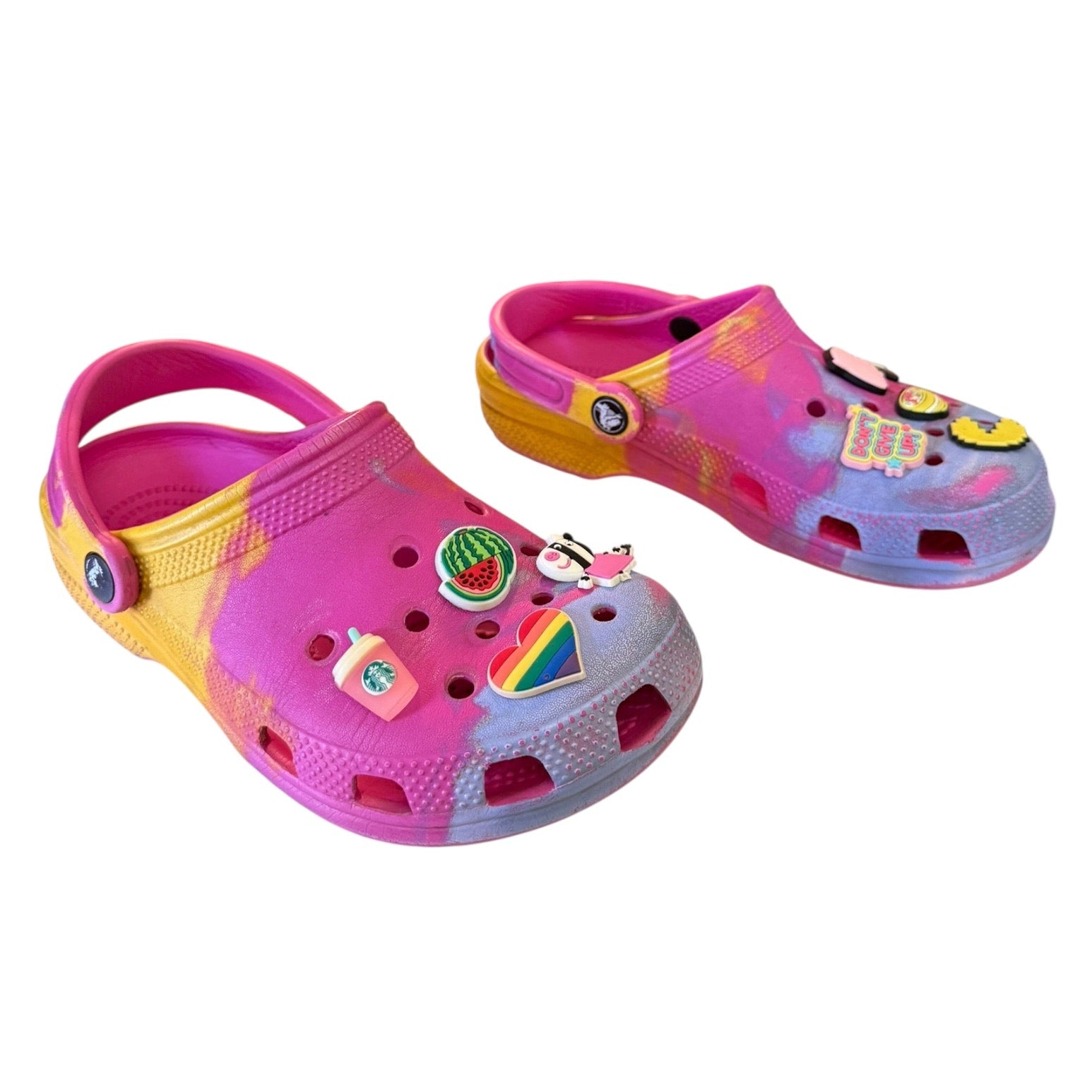 Pair of pink and yellow clogs with decorative charms on a white background