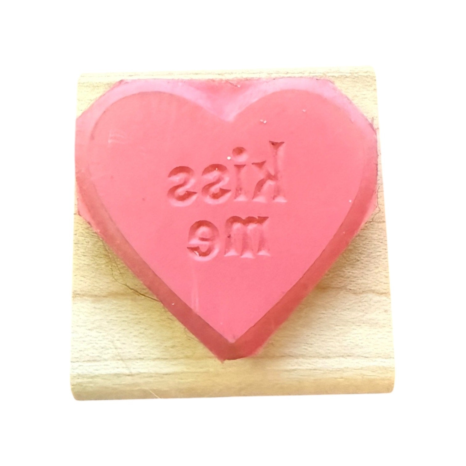 Pink heart-shaped rubber stamp with 'kiss me' text on a wooden block