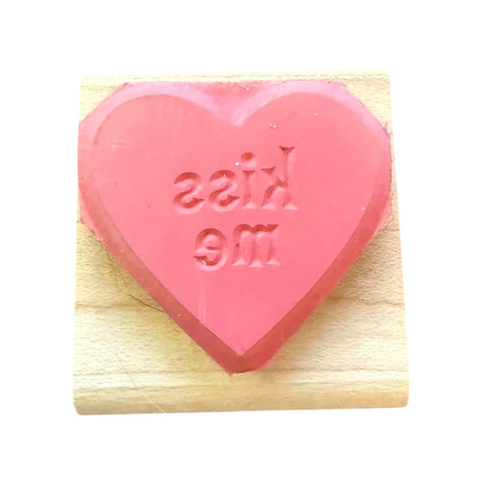 Pink heart-shaped rubber stamp with 'kiss me' text on a wooden block
