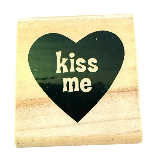 Wooden block with a black heart-shaped cutout and 'kiss me' text on a white background