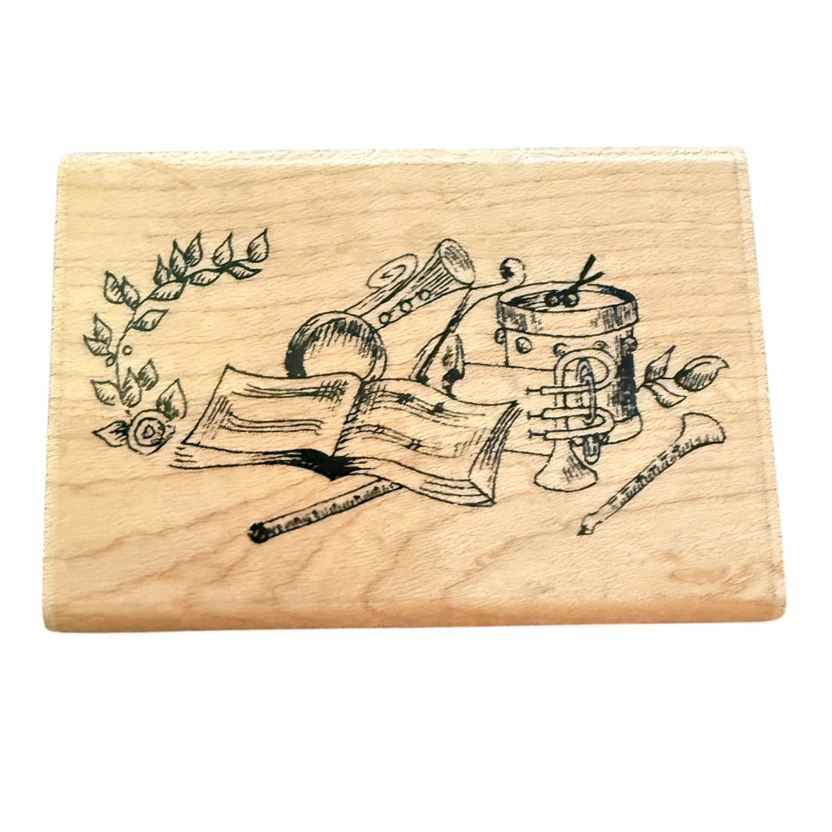 A rectangular wooden stamp featuring a black illustration of musical instruments, including a trumpet, drum, flute, and a rose branch, on a light wood grain surface.