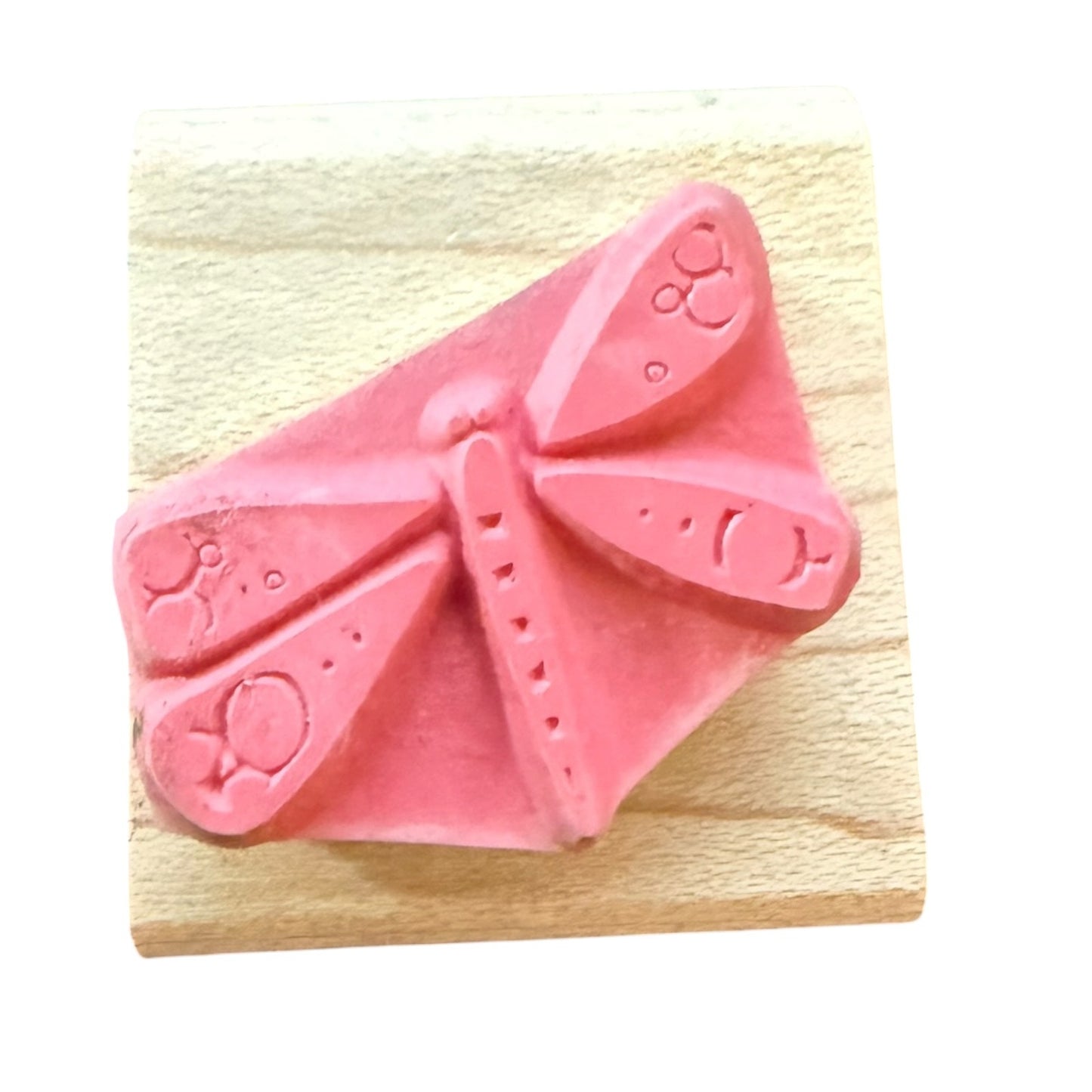 A pink rubber stamp featuring a dragonfly design, mounted on a light-colored wooden block against a white background.