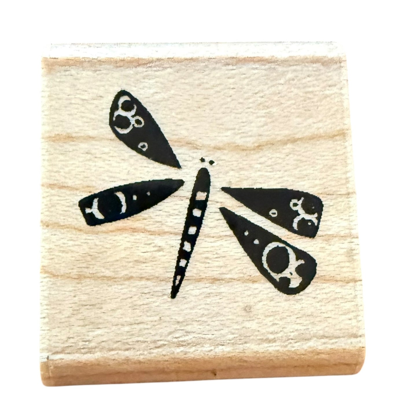 A square wooden rubber stamp block featuring a black dragonfly design with white circular details, isolated on a white background.