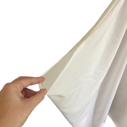 A hand holding the sleeve of a white swimsuit cover up,  against a plain white background.