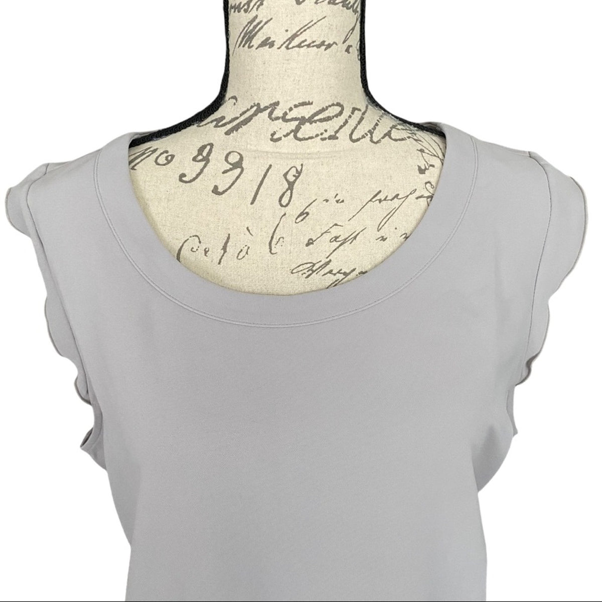 A light gray top with ruffled cap sleeves, displayed on a vintage-style fabric dress form with cursive script print.
