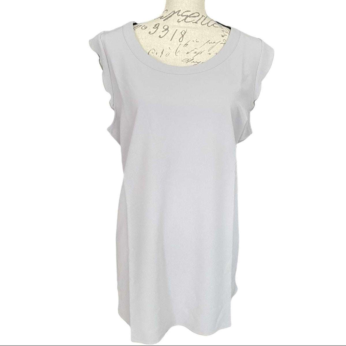 A light gray sleeveless top with ruffled cap sleeves, displayed on a cream-colored dress form against a white background.
