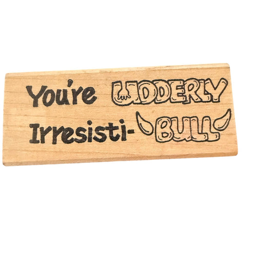 A rubber stamp with engraved black text reading 'You're UDDERLY Irresisti-BULL!'.