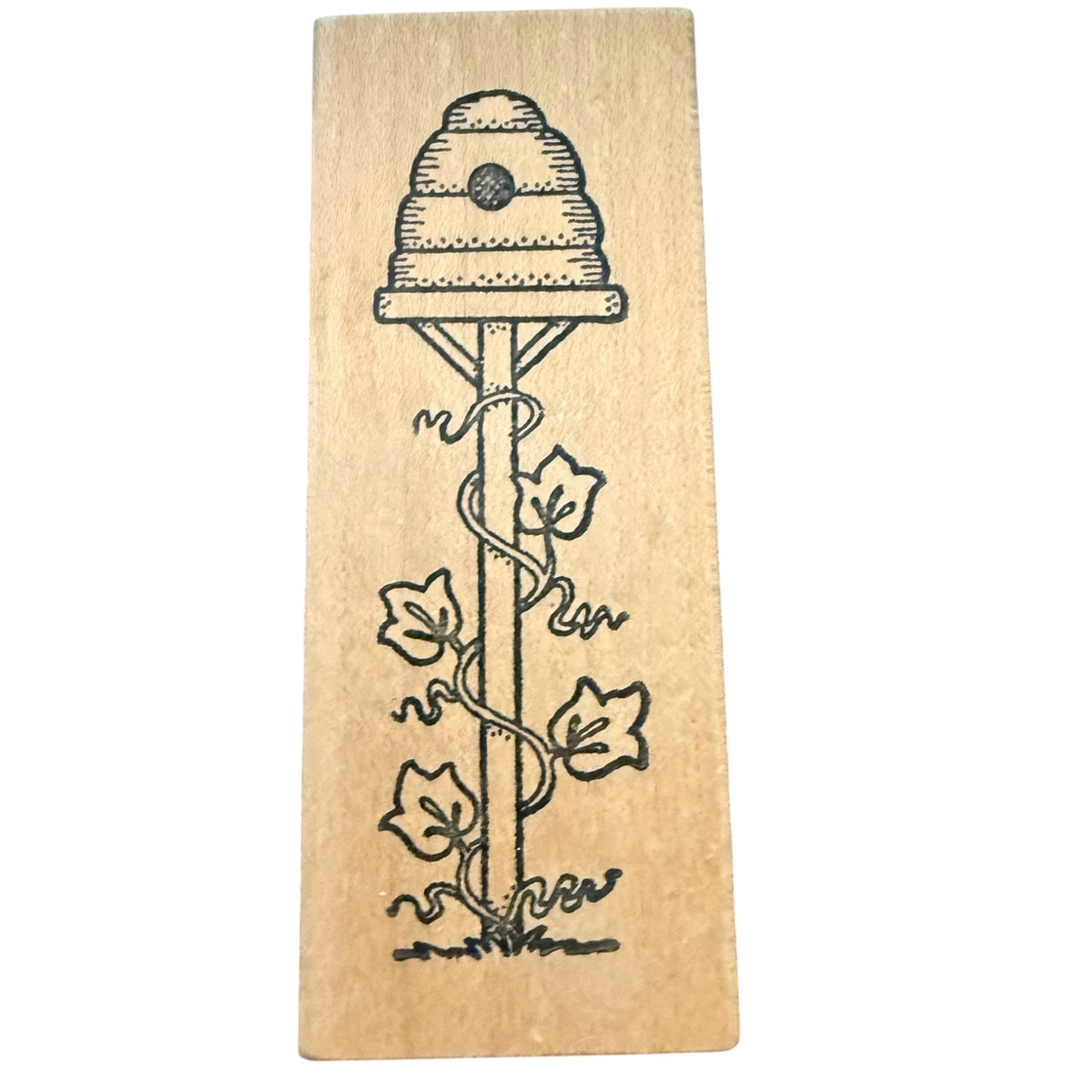 A rectangular wooden stamp block featuring a black ink illustration of a beehive with climbing vines and leaves, shown against a plain white background.