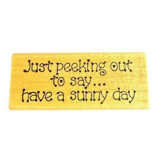 Wooden block with black text 'Just peeking out to say... have a sunny day' on a white background