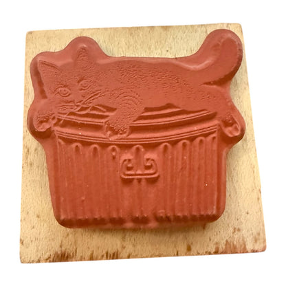 Rubber stamp of a cat on a trash can on a wood block