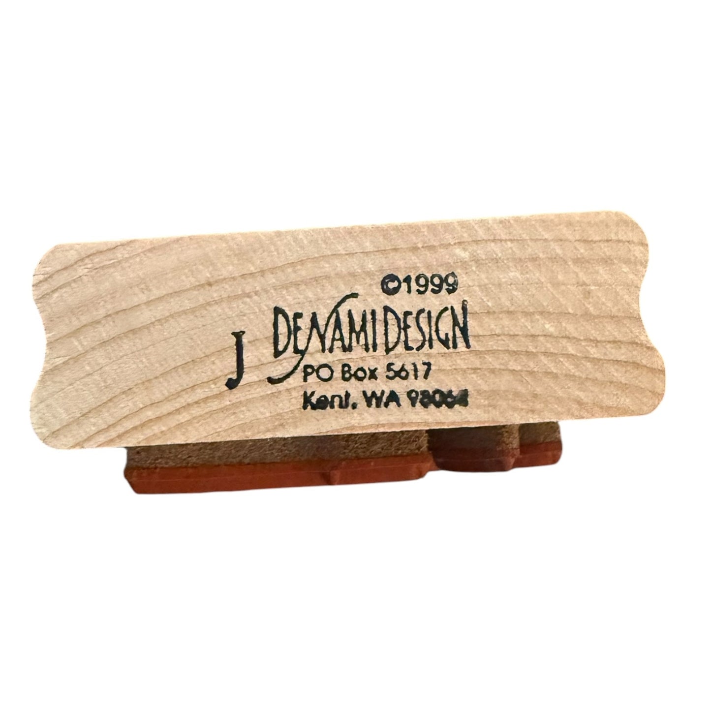 A small carved wooden block with rounded corners, shown on a plain white background. The front is light natural wood with black printed text 