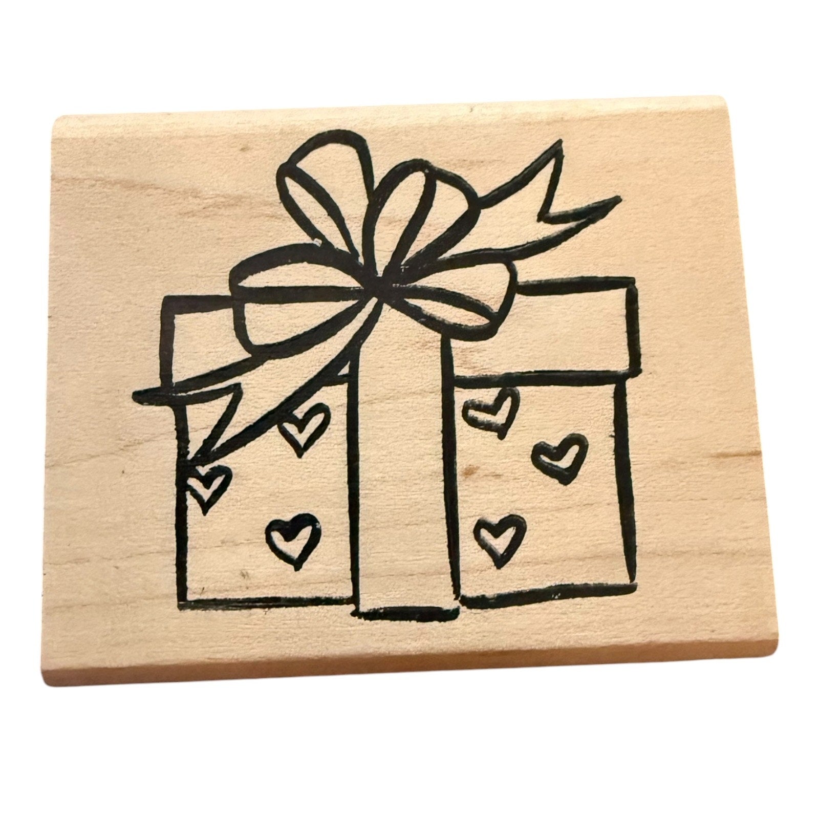 A square wooden stamp block featuring a black line-art design of a gift box with a bow and small hearts, shown on a plain white background.